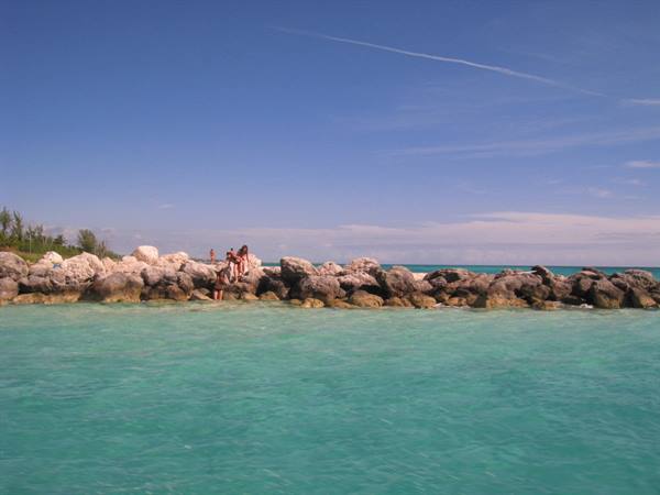 People sitting on white rocks between turquoise water and blue sky