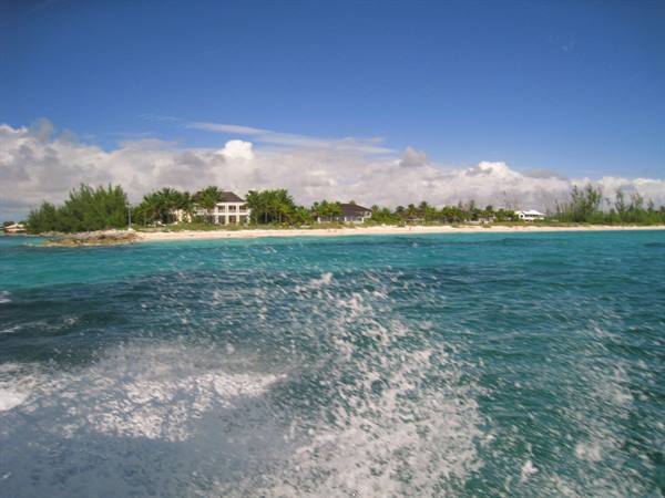 Boat wake on turquoise water near beach with villas and palms