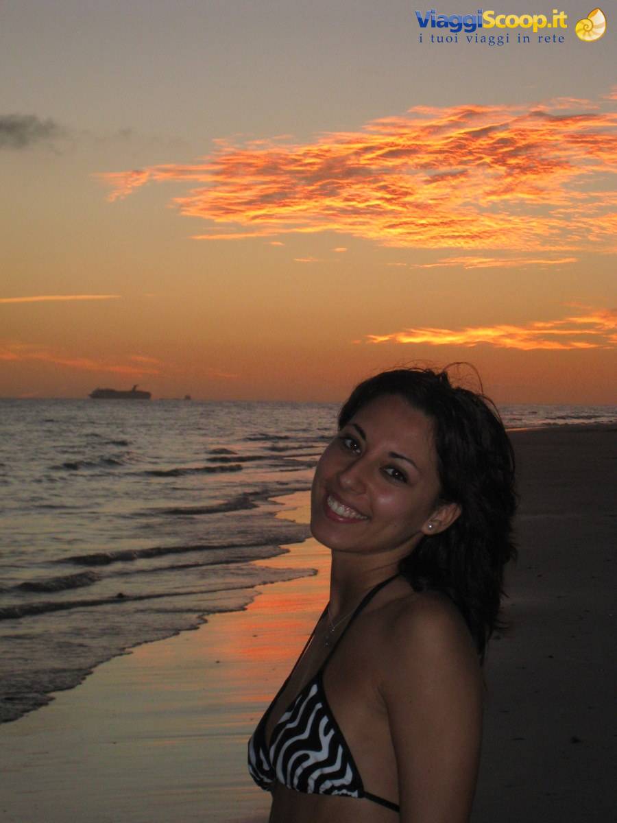 Smiling woman in bikini on beach at dusk, ships on the horizon