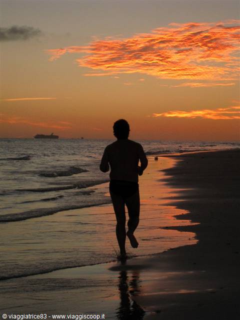 Man running barefoot along the shoreline at dusk, ship offshore