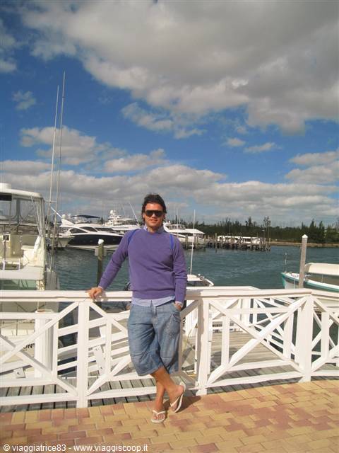 Man in purple sweater leaning on white railing in front of yachts at the marina