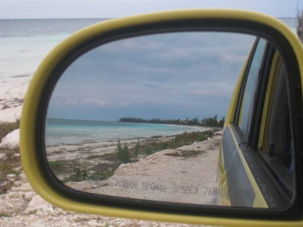 Yellow car side mirror reflecting sandy beach and turquoise sea