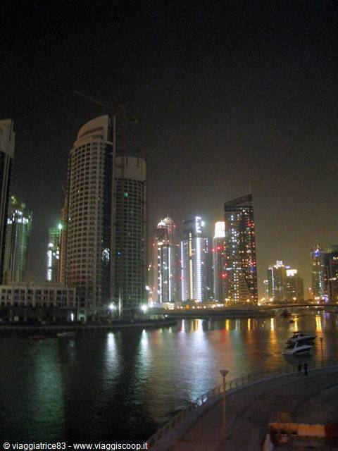 Illuminated Dubai Marina skyscrapers reflected in the water at night, moored yacht