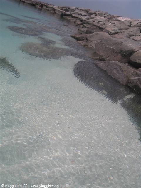 Clear turquoise water over sand beside grey boulders