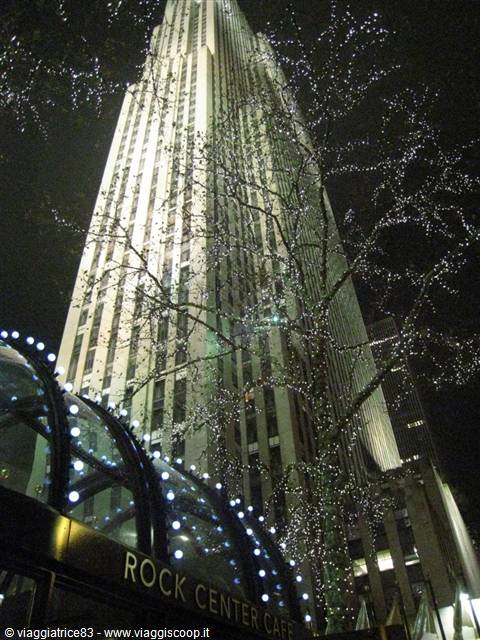 Rockefeller Center at night: lit skyscraper, tree with Christmas lights, cafe entrance
