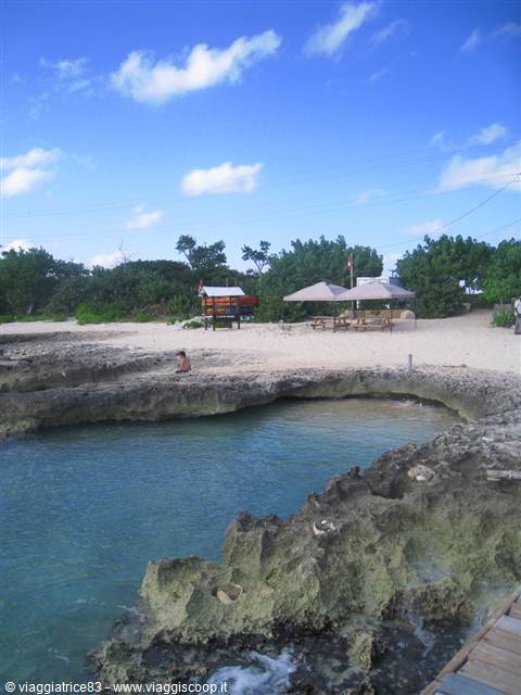 Sandy beach with umbrellas and tables among coral rocks and turquoise water