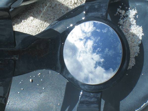 Black snorkel mask on white sand reflecting the cloudy sky