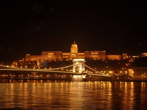 Buda Castle lit up above the Chain Bridge, golden reflections on the Danube at night
