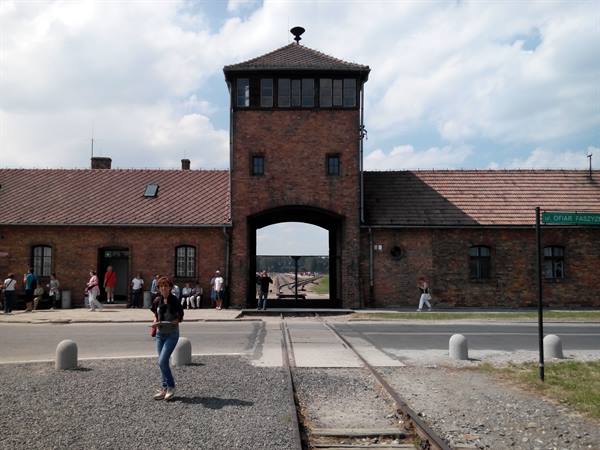 Tourist walks past the brick watchtower and railway tracks at Birkenau
