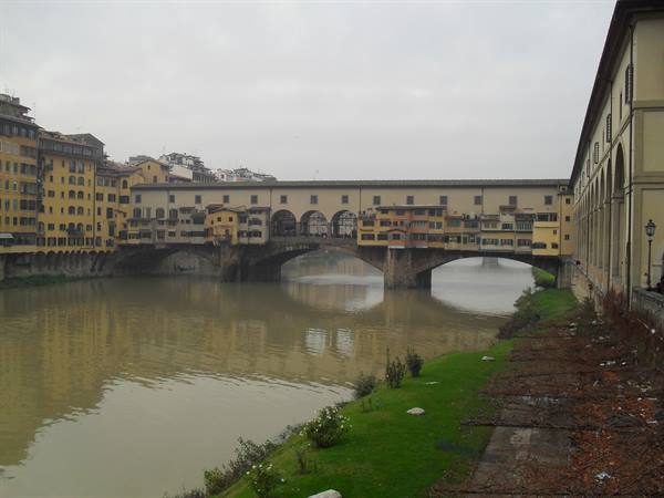 Ponte Vecchio with its shops crosses the Arno under a gray sky