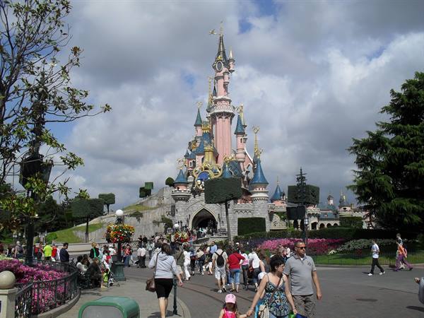 Visitors walk in front of the Sleeping Beauty Castle at Disneyland Paris under clouds