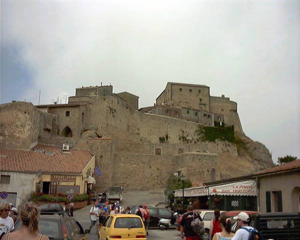Tourists and cars in the square beneath Capalbio's medieval stone hilltop village