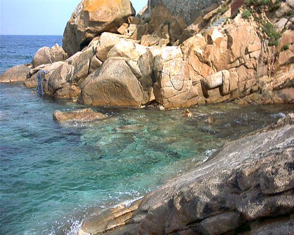 Clear turquoise water among large granite boulders, metal ladder on the rock
