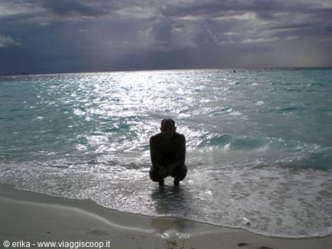 Man crouching in clear turquoise water on a tropical beach under cloudy skies