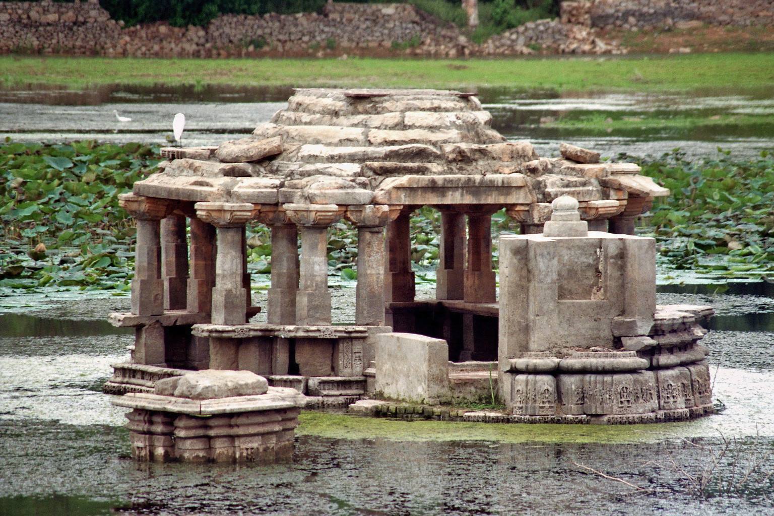 Ancient stone temple submerged in a lotus pond with carved pillars and an egret