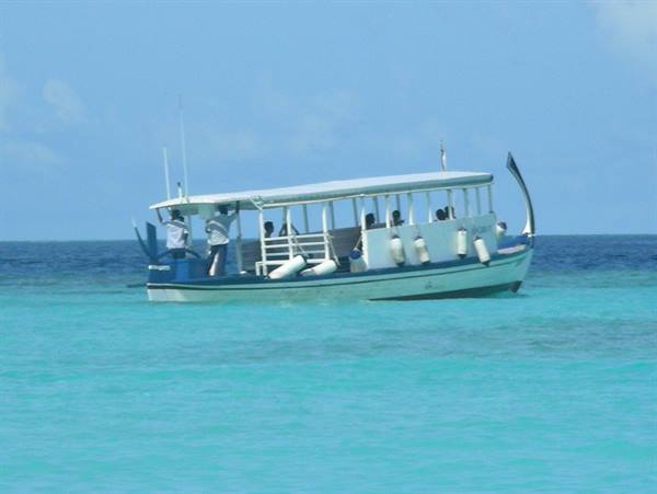 White dhoni carrying tourists and oxygen tanks glides across turquoise water