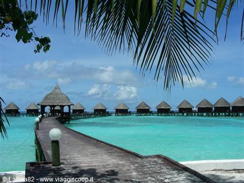 Wooden pier over turquoise water leading to overwater bungalows and thatched pavilion