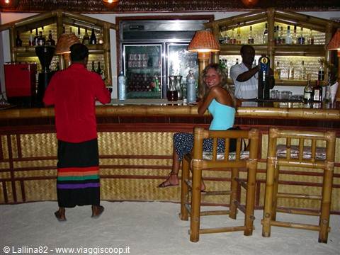 Woman seated at bamboo bar counter, bartender behind, warm lamp light