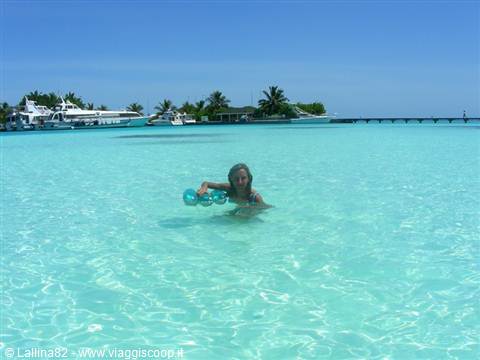 Child swims in turquoise lagoon with float rings, yachts and palms on jetty