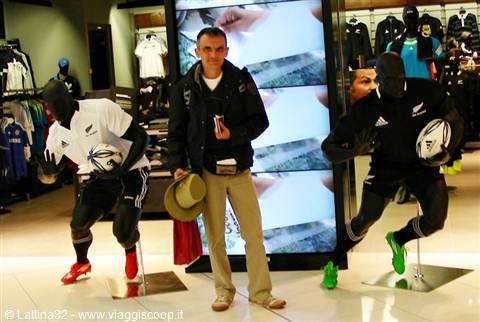 Man in store among All Blacks rugby mannequins beside bright screen