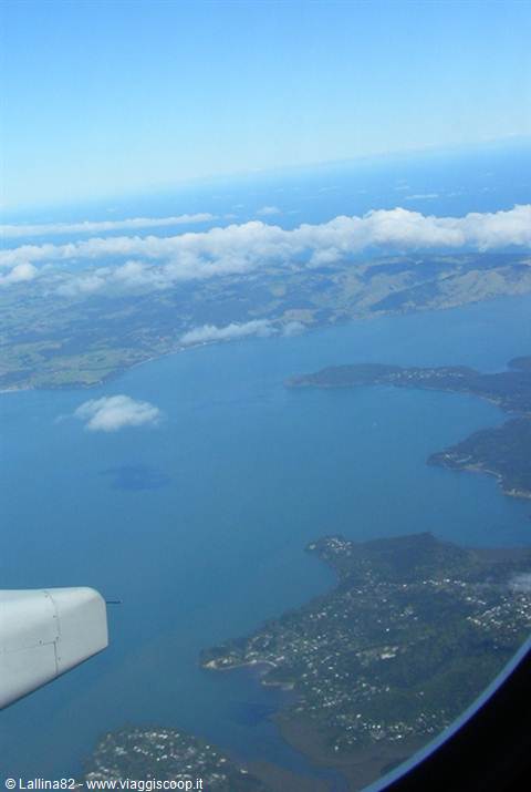 From the plane window, the engine above a blue bay and green coastline