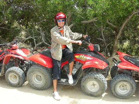 Kid in red helmet and sunglasses sitting on a red quad bike among trees