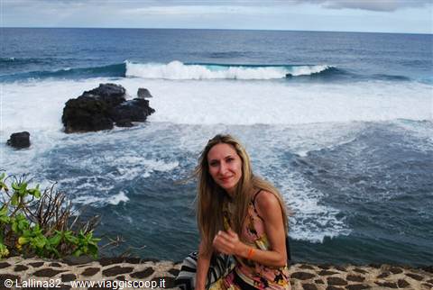 Woman sitting on volcanic stone wall with waves breaking on black rocks