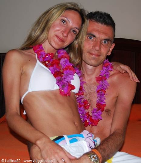 Couple in swimwear wearing pink and purple flower leis, sitting on bed