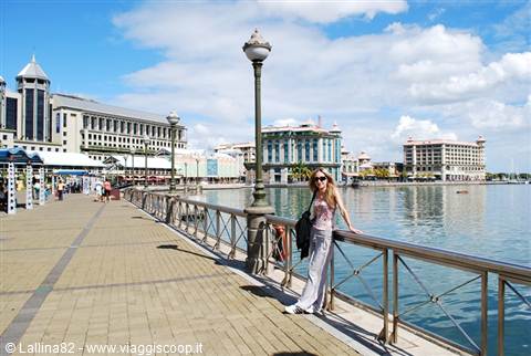 Traveler on Port Louis waterfront, blue water and colonial buildings under white clouds