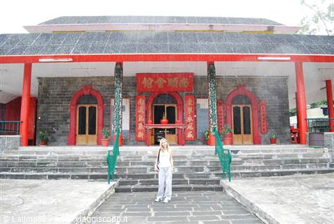 Tourist standing on the steps of a Chinese temple with volcanic stone walls and red gates