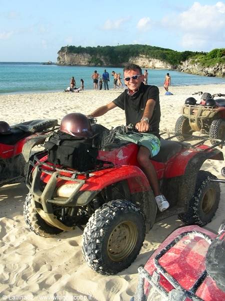 Man in sunglasses riding a red quad bike on a sandy beach