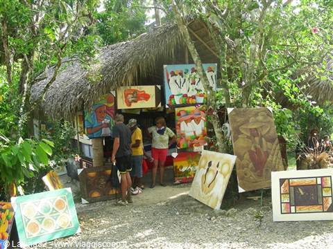 Visitors browse colorful paintings displayed outside a thatched-roof hut