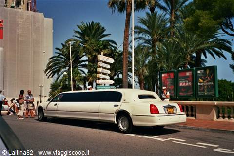 White stretch limousine parked under palm trees among pedestrians downtown