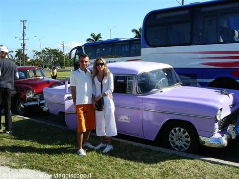 Couple beside a vintage lilac Chevrolet parked near tour buses