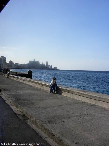 Couple embracing on Havana's Malecón seawall, blue ocean, clear sky