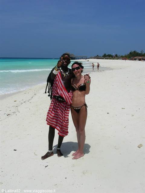 Tourist in bikini next to a Maasai man in red cloth on white sand