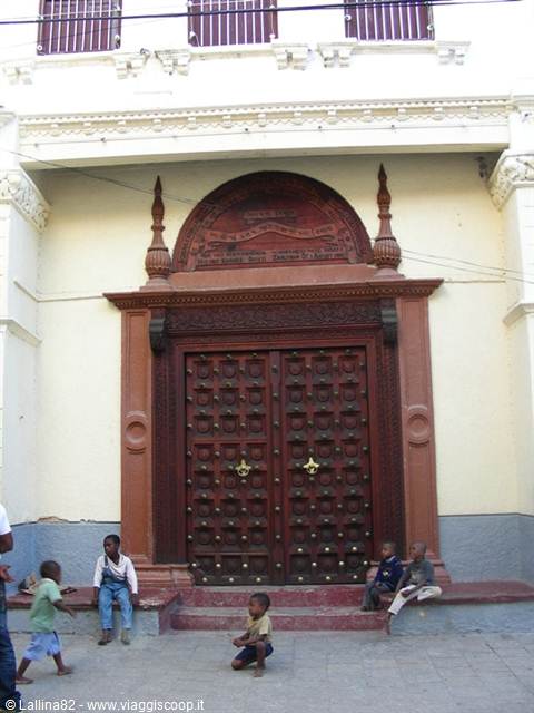 Children sitting on the steps of a large carved dark wooden doorway