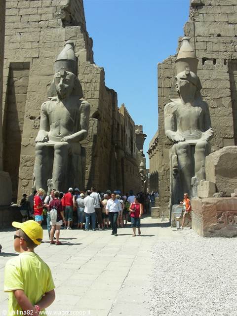 Tourists walking between seated Ramses II statues at Luxor Temple