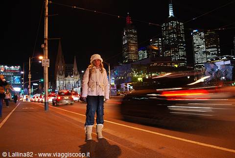 Tourist in white coat crossing a busy night street among Melbourne skyscrapers