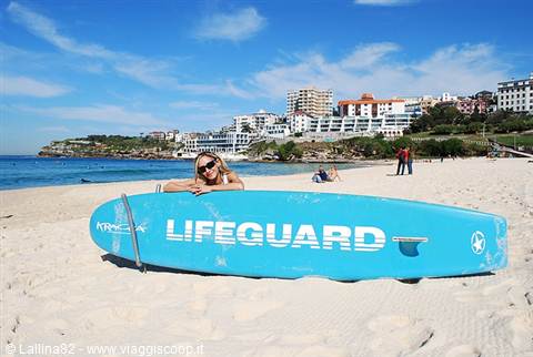 Woman in sunglasses leaning on a blue lifeguard board on the sand