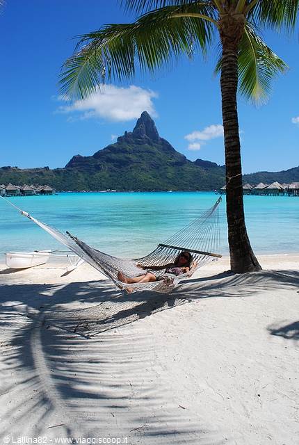 Woman resting in a hammock under palms, white sand and turquoise lagoon, Bora Bora