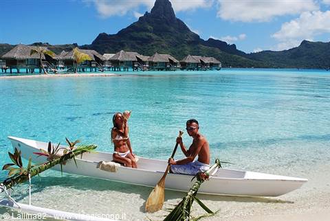 Couple on white canoe in Bora Bora turquoise lagoon with overwater bungalows
