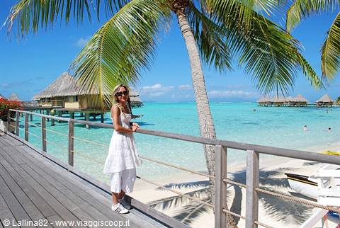 Woman in white on wooden boardwalk among palms and overwater bungalows