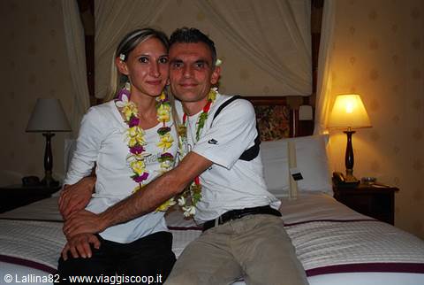 couple wearing flower leis on a hotel bed, lamps lit