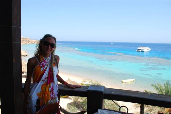 Woman in floral sarong and sunglasses beside a turquoise lagoon with boats