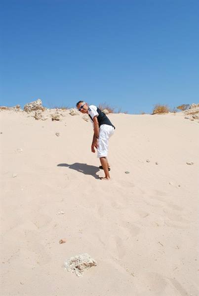 Man in white shorts bending down on a sandy dune