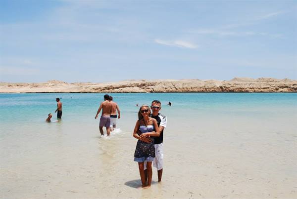 Couple standing in turquoise water at Nazaré beach, rocky cliffs behind