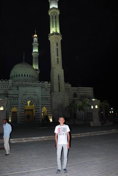 Tourist in white t-shirt in front of the illuminated Al Sahaba Mosque at night