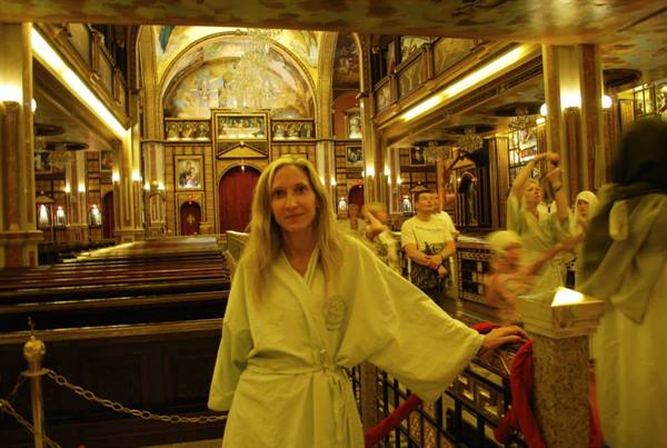 Woman in light robe inside an Orthodox church with golden mosaics and icons