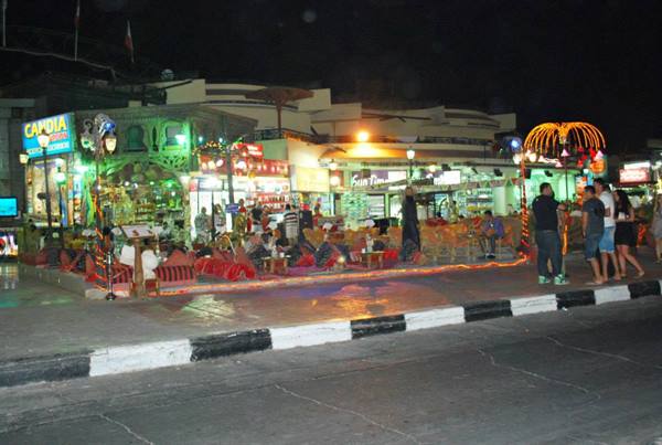 Night-lit café with people seated on cushions and carpets along the street